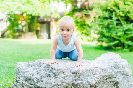 Outdoor portrait of a cute toddler boy claiming on a big stone at the parkの写真素材
