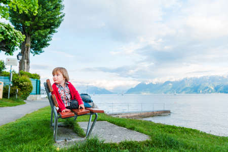 Cute toddler boy resting on a bench next beautiful lake on a nice summer eveningの写真素材