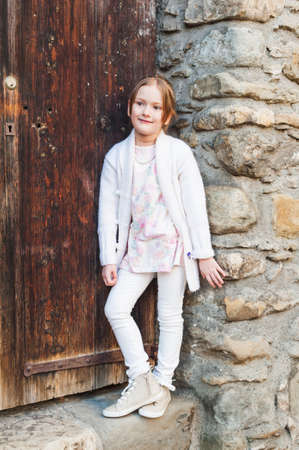 Cute little girl posing outdoors against wooden door, wearing white clothesの写真素材