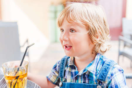 Adorable toddler boy drinking apple juice in a cafeの写真素材