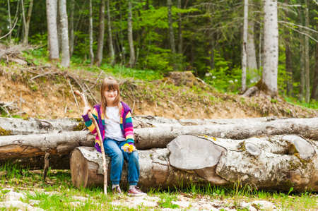 Outdoor portrait of a cute little girl, sitting on a fallen tree in a forest on a nice sunny dayの写真素材