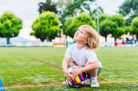 Cute toddler boy playing with a ball on a stadiumの写真素材