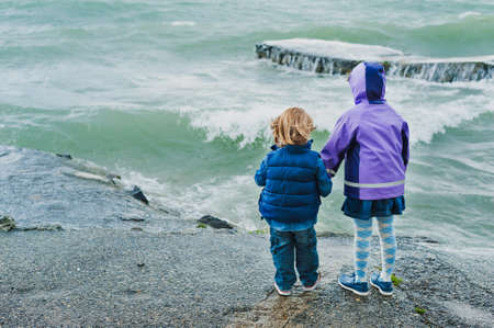 Adorable children playing next to lake on a stormy day, back viewの写真素材