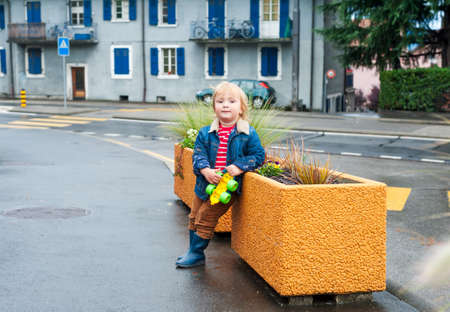 Outdoor portrait of a cute toddler boy in a city after rainの写真素材