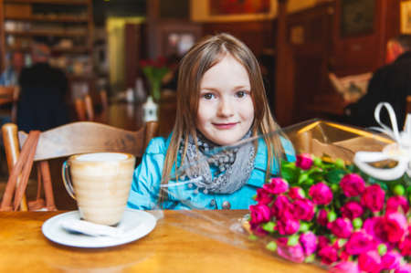 Cute little girl in a cafe with cup of hot chocolate and bouquet small pink roses, interior portraitの写真素材