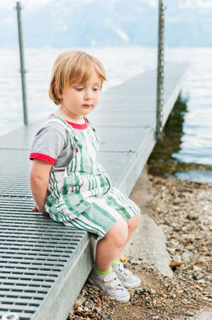 Outdoor portrait of a cute toddler boy sitting on a pierの写真素材