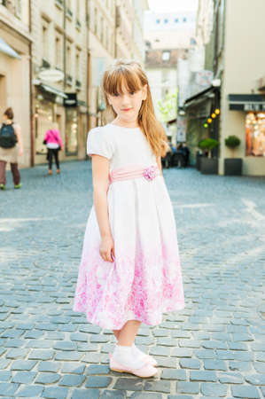 Outdoor portrait of a cute little girl in a beautiful dress in a cityの写真素材