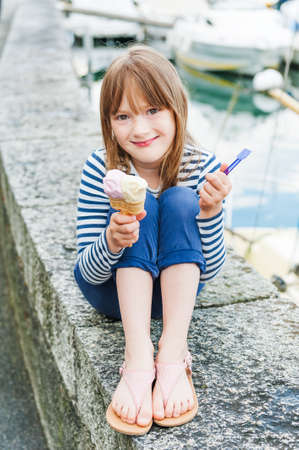 Outdoor portrait of a cute little girl, eating ice cream in a portの写真素材