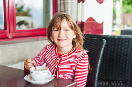 Cute little girl drinking hot chocolate in a cafeの写真素材