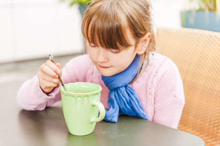 Outdoor portrait of a cute little girl drinking hot chocolate in a cafeの写真素材