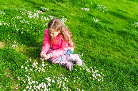 Beautiful little girl playing with flowers in a park on a nice sunny day in a early spring, wearing bright pink jacketの写真素材
