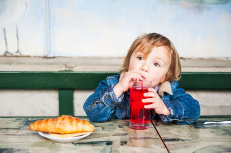 Cute toddler boy having a snack on a terrace in a cafeの写真素材