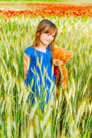 Summer portrait of a cute little girl playing with teddy bear in a wheat fieldの写真素材
