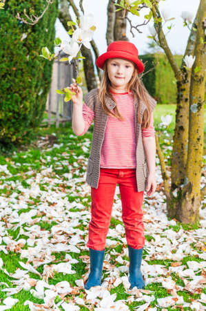 Spring portrait of a cute little girl in a red had next to magnolia treeの写真素材