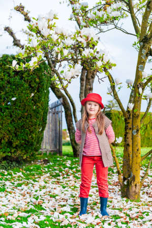 Spring portrait of a cute little girl in a red had next to magnolia treeの写真素材