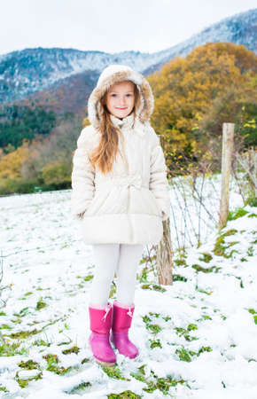 Winter portrait of a cute little girl in a white jacket and pink bootsの写真素材