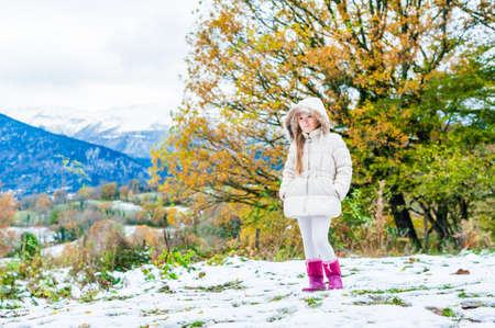 Winter portrait of a cute little girl in a white jacket and pink bootsの写真素材