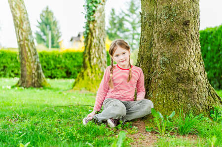 Adorable little girl sitting under the tree on a nice sunny dayの写真素材