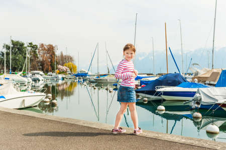Cute little girl resting next to lake, weraing red and white top and jeans skirtの写真素材