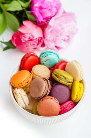 Colorful macaroons in a bowl with peonies on a white backgroundの写真素材