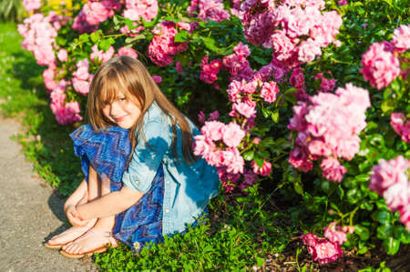 Portrait of a cute little girl on sunset, sitting next to beautiful rose bushesの写真素材