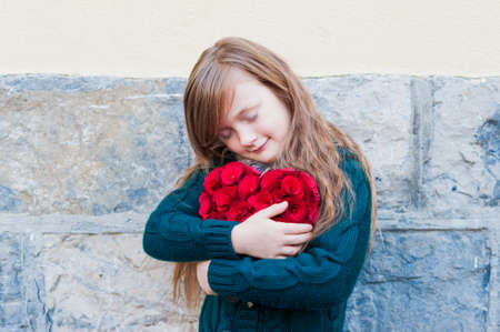 Cute little girl hagging big red heart with eyes closedの写真素材