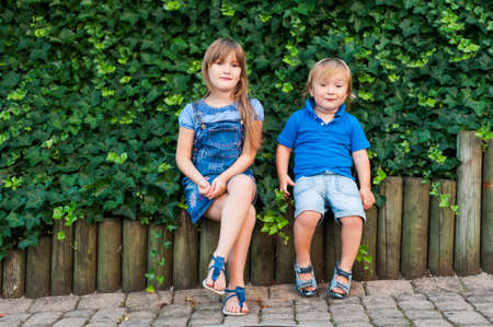 Summer portrait of a toddler brother and big sister, sitting next to green ivy, wearing, blue clothesの写真素材
