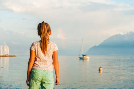 Cute little girl looking at the beautiful lake on sunsetの写真素材