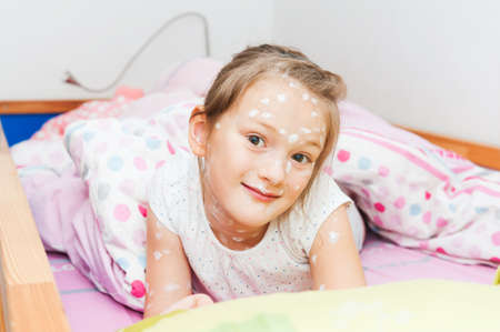 Little girl of 7 years old with chicken pox resting in a bedの写真素材