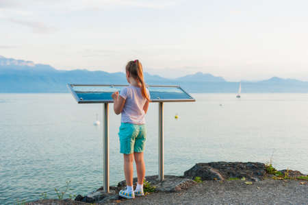 Little girl reading a map with Haute-Savoie Alps, standing by the lake Geneva in the eveningの写真素材