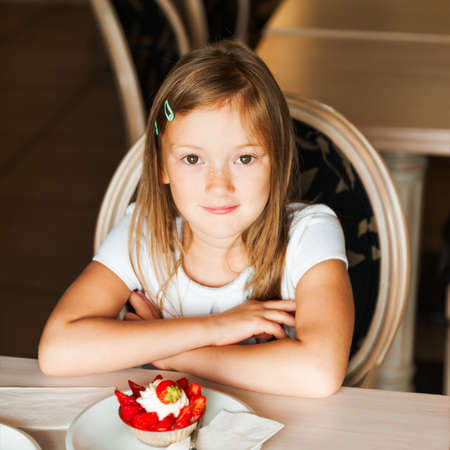 Cute little girl eating strawberry cake in a cafeの写真素材