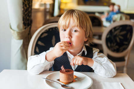 Adorable toddler boy eating chocolate cake in a beautiful cafeの写真素材