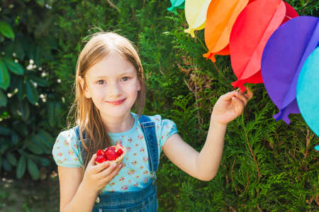 Adorable little girl eating strawberry cake on a birthday party on a nice sunny summer dayの写真素材