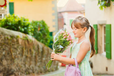 Outdoor portrait of a cute little girl with beautiful bouquet of pink rosesの写真素材