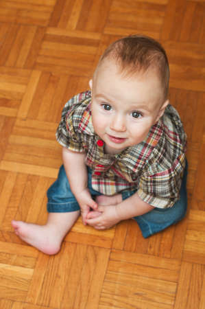 Interior portrait of a cute baby boy sitting on the wooden floor at homeの写真素材