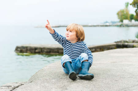 Cute toodler boy having fun outdoors, playing next to lake on a rainy dayの写真素材