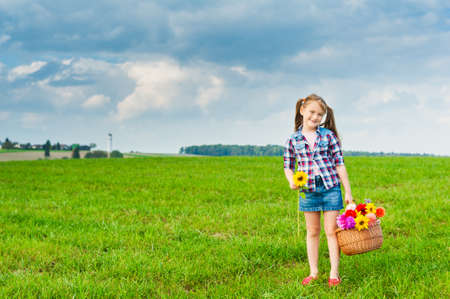 Outdoor portrait of adorable little girl playing with flowers in a field in countryside on a nice sunny dayの写真素材
