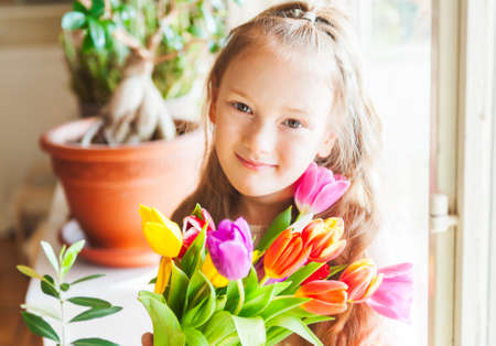 Romantic portrait of adorable little girl with colorful tulips, indoorsの写真素材