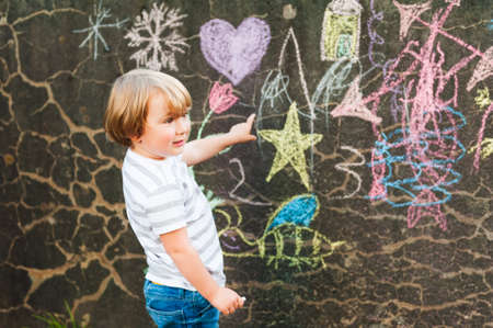 Cute toddler boy drawing with chalk on a nice day outdoors