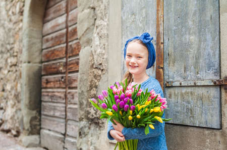 Outdoor portrait of a cute little girl in an old city with huge bouquet of colorful fresh tulipsの写真素材