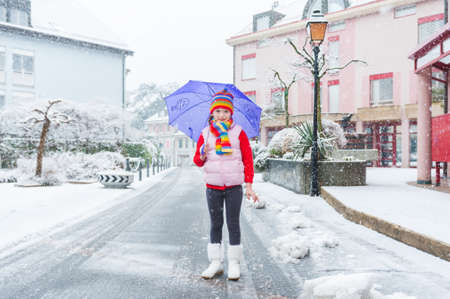 Outdoor portrait of a pretty little girl in a city under the snowfallの写真素材