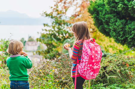 Two adorable kids having a snack outdoors after school, eating sugar bread in the parkの写真素材