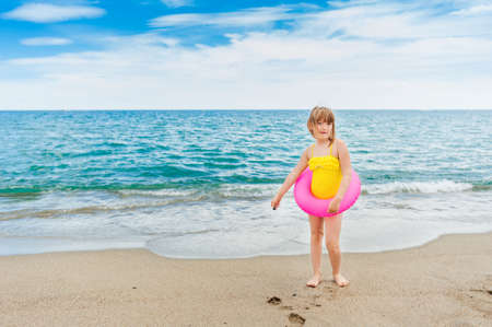 Adorable little girl with pink inflatable ring by the sea on summer vacationの写真素材