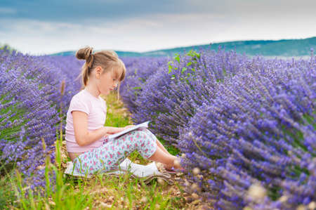 Adorable little girl reading a book in a lavender field on a nice sunny eveningの写真素材