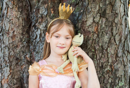 Cute little girl playing with a toy frog, pretending to be a princessの写真素材