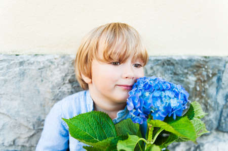 Close up portrait of a cute blond toddler boy playing with a big beautiful flower outdoorsの写真素材