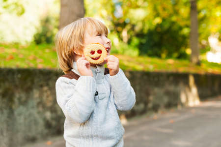 Outdoor portrait of adorable toddler boy in autumn park, having fun and eating a biscuitの写真素材