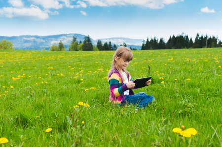 Cute little girl playing with tablet pc outdoorsの写真素材