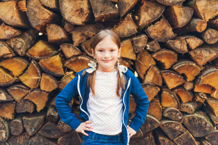 Cute little girl with pigtails standing against of a background with firewoodの写真素材