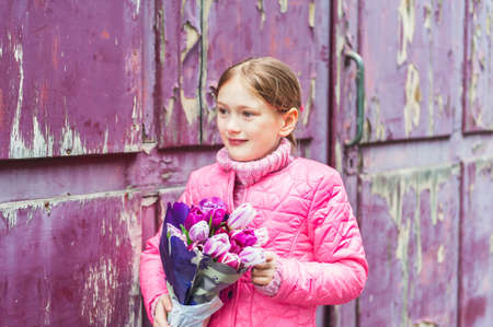 Spring portrait of adorable little girl of 7 years old, wearing bright pink coat, holding beautiful bouquet of tulipsの写真素材
